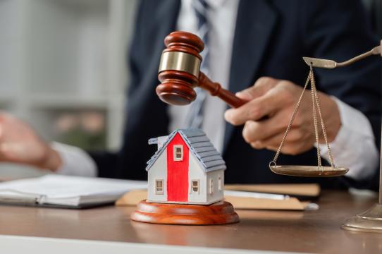 A judge strikes a gavel beside a small house model, symbolizing property law, housing disputes, or real estate judgment