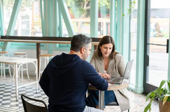 a man and a woman sitting at a table looking at a laptop