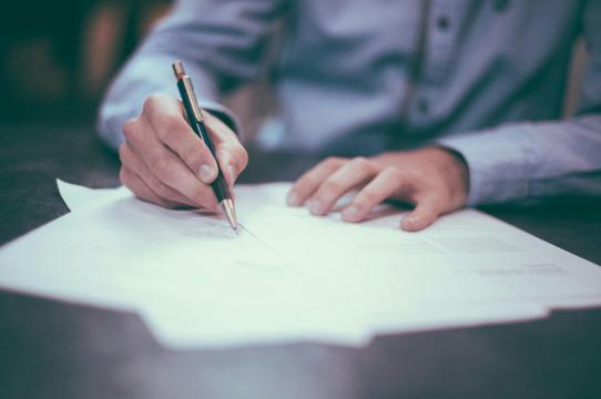 person signing holding a pen signing a paper
