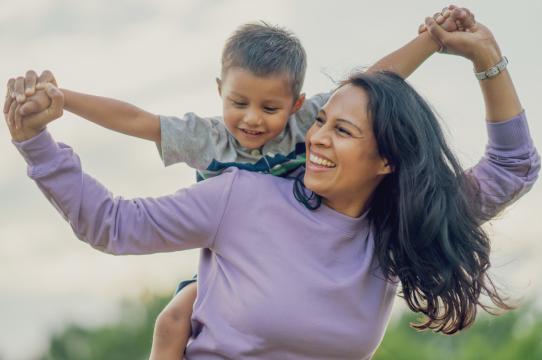 A smiling mother gives her son a piggyback ride outdoors.