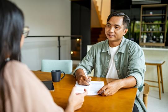 A man reviews and signs paperwork while meeting with an advocate
