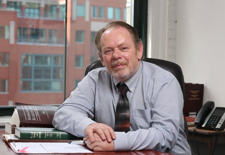 Photo of Brian wearing a suit and sitting at a conference table with a stack of legal books and documents